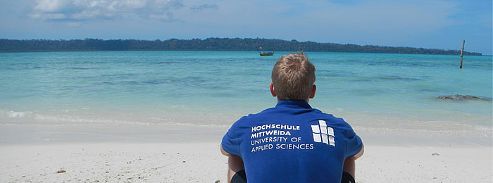 Studierender sitzt am Strand und blickt auf das Meer