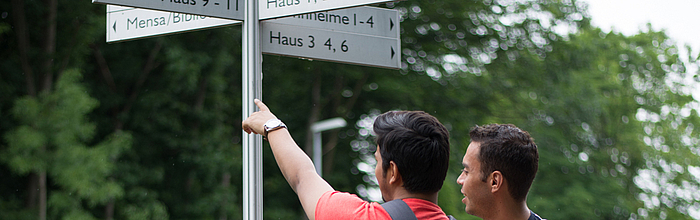 Internationale Studierende betrachten eine Wegweiser auf dem Campus