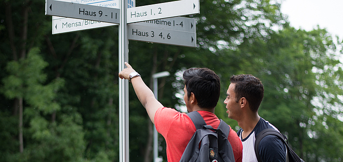 Internationale Studierende betrachten eine Wegweiser auf dem Campus